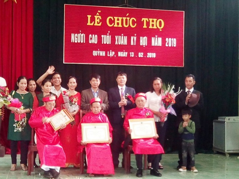 Đồng chí Hồ Sỹ Hoàng, Bí thư Đảng ủy, Chủ tịch HĐND xã và các đồng chí trong Ban Thường vụ tặng áo lụa đỏ cho các cụ 90 tuổi